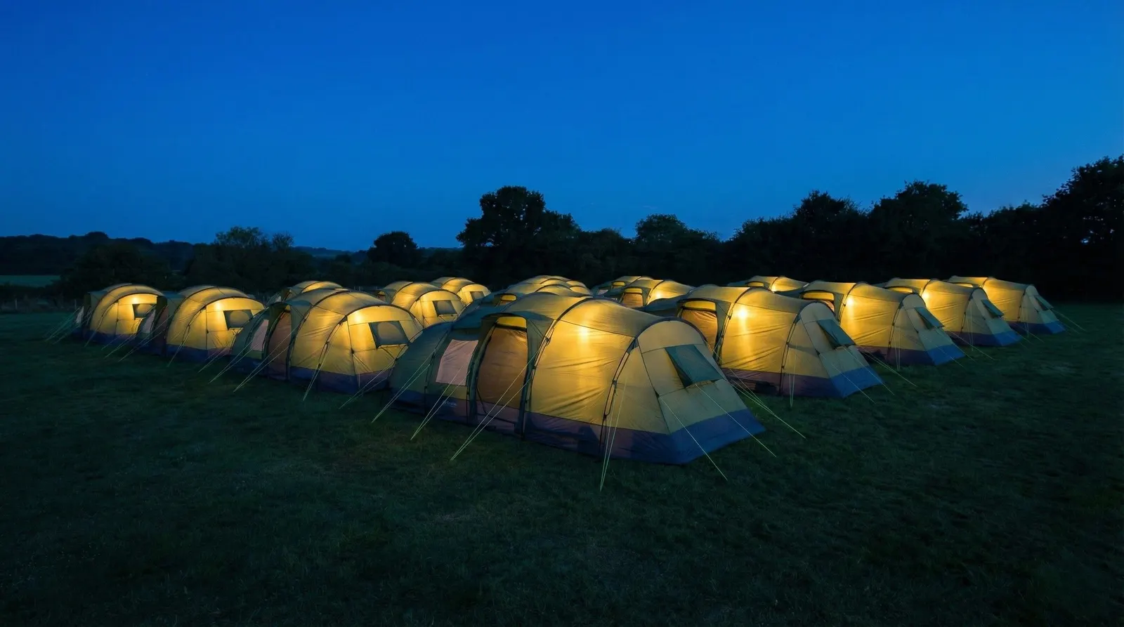 Pre-pitched ZIP tent village glowing at twilight at a festival
